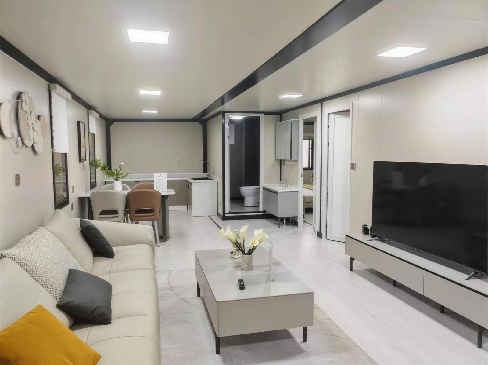 Open-plan living and dining area inside an Expandable Home, with a cream leather sofa and compact kitchenette.