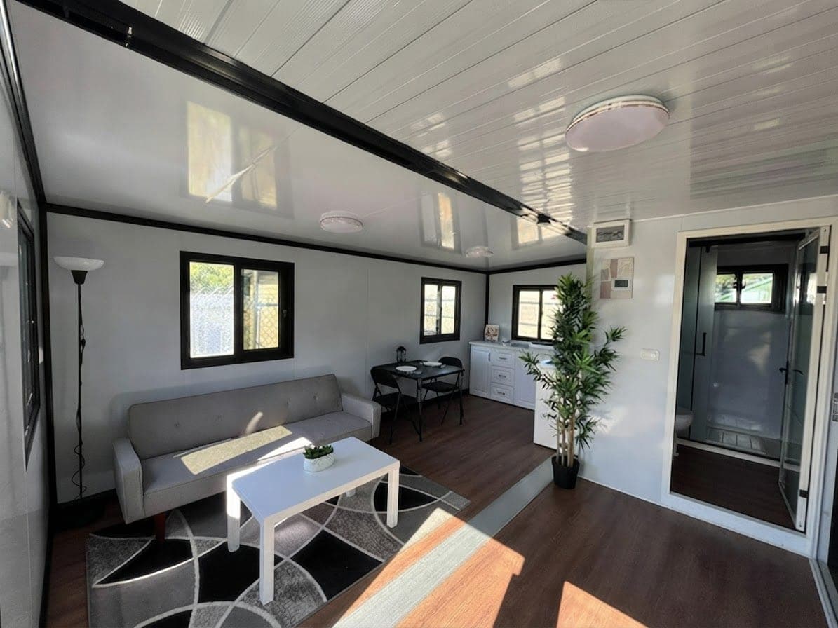 Expandable home lounge interior with grey sofa, white coffee table, dining nook and kitchenette on wood-look flooring
